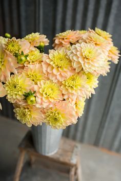 a vase filled with yellow and pink flowers sitting on top of a wooden table next to a metal wall