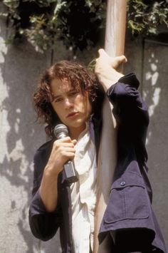 a man holding a microphone up to his face while standing next to a pole with trees in the background