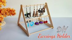 a wooden jewelry holder with earrings hanging from it's sides and an orange flower in the background