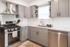 a kitchen with stainless steel appliances and white tile flooring, along with gray cabinets