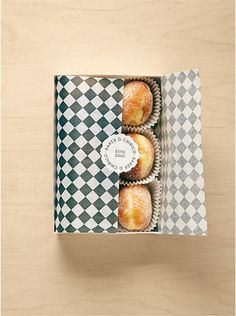 three donuts in a box on top of a wooden table with checkered paper