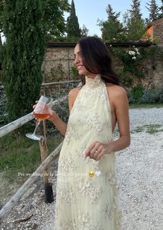 a woman in a dress holding a wine glass and looking at the camera while standing outside