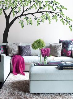 a living room with a tree painted on the wall and white couches, coffee table