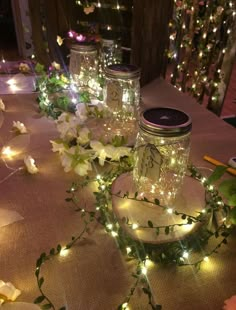 some mason jars are sitting on a table with flowers and fairy lights around the jar