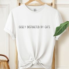 'Easily Distracted By Cats' White Unisex Softstyle T-Shirt. This unisex softstyle tee is made from high-quality materials and is available in a variety of sizes.  It is made with ring-spun cotton, a lightweight fabric, and is the comfiest shirt you will own!   CHOOSING A SIZE Please check the size guide in the listing images carefully and be sure to measure yourself before placing an order. All our items are made to order, and so we are unable to accept returns due to ordering the wrong size. Pl Casual Cat Design T-shirt As Gift, Spring White T-shirt With Cat Design, Cat Tshirts Funny, Funny White T-shirt With Cat Design, Cheap Playful T-shirt With Cat Design, Funny Short Sleeve T-shirt With Cat Design, Easily Distracted, Comfy Shirts, Cat T