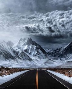 an empty road with snow on the ground and mountains in the background