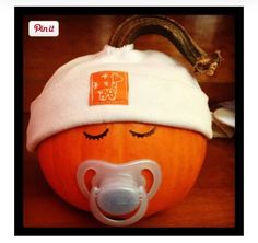 an orange pumpkin with a pacifier attached to it's side and a white hat on top