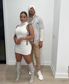 a man and woman standing next to each other in front of a white wall wearing all white