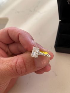 a person holding a ring with a diamond in it's middle and an empty box on the other side