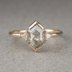 an engagement ring with two diamonds on the side and one diamond in the middle, sitting on top of a gray surface