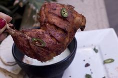 a person holding up a piece of meat in a cup with sour cream and jalapenos