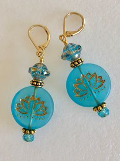 "Lovely aqua blue Czech glass lotus flower earrings with gold Picasso wash. These are large 22mm flat coin beads in a transparent matte aqua blue with same design on each side. Accented with transparent Czech glass saucer beads with mottled gold finish. All Premium Czech glass beads. Additional accents include ornate Antique gold pewter spacers and small aqua Czech rondelles. Earrings are on gold plated lever backs and are 2\" long." Blue Round Beads Spiritual Earrings, Blue Spiritual Earrings With Round Beads, Blue Spiritual Earrings For Gifts, Turquoise Czech Glass Flower Earrings For Gift, Blue Round Flower Earrings Hypoallergenic, Blue Round Hypoallergenic Flower Earrings, Blue Spiritual Nickel-free Earrings, Hypoallergenic Blue Flower Earrings, Blue Round Flower Earrings With Ear Wire