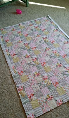 a patchwork quilt laying on the floor next to a green chair and pink flower