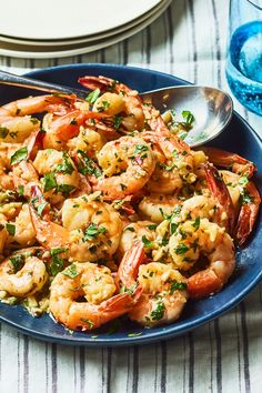 a blue plate topped with cooked shrimp and garnished with parsley next to a glass of water