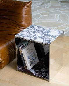 a marbled end table with magazine rack on it in front of a brown leather chair