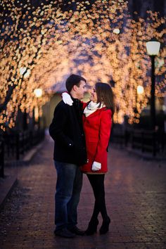 a man and woman standing next to each other in front of trees with lights on them