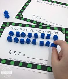 two hands are holding blue and green cubes in front of a white sheet that says build & solve the fraction