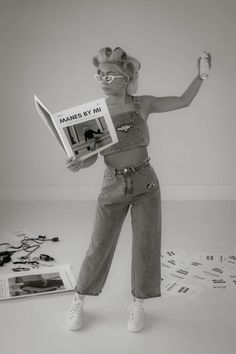 a black and white photo of a woman holding a magazine in one hand while standing on the floor