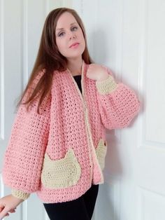 a woman wearing a pink crochet jacket standing next to a door with her hands on her hips