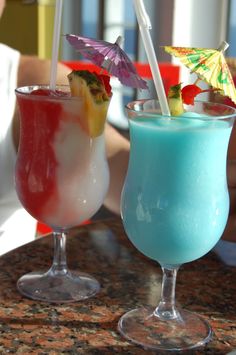 two glasses filled with different colored drinks on top of a marble counter next to each other