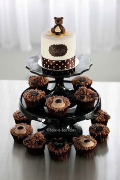 a three tiered cake with cupcakes on the bottom and a teddy bear on top