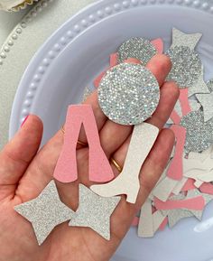 a person holding some glittered letters in their hand on a plate with flowers and cupcakes