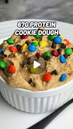 a cookie dough with m & m cookies in it on a white plate next to a fork