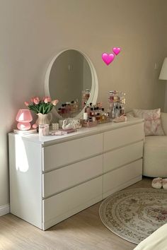 a white dresser sitting next to a bed with pink hearts on it's mirror