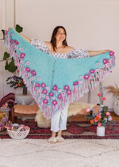 a woman standing in front of a rug holding a blue shawl with pink flowers on it