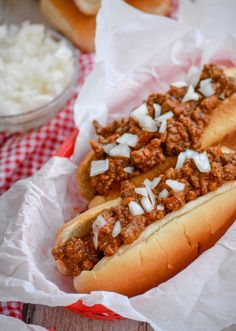 two chili dogs in buns with onions and cheese on the top, sitting next to a bowl of rice