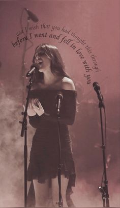 a woman singing into a microphone in front of two microphones with writing on the wall behind her