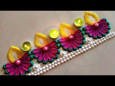 three colorful flowers with pearls and beads on a white table top next to a candle holder