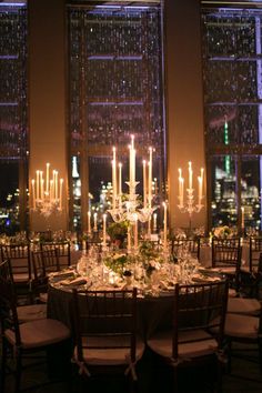 a dining table with candles and flowers in front of two large windows overlooking the city at night