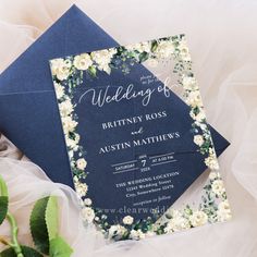 a blue and white wedding card with flowers on it next to a bouquet of greenery