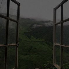 an open window looking out onto a lush green valley with mountains in the distance on a foggy day