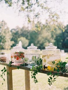 several jars with flowers and leaves are lined up on a wooden table in the grass