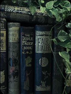 several books are lined up on a shelf next to some plants and ivy growing in front of them