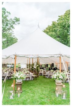 an outdoor tent set up for a wedding reception with candles and flowers on the tables