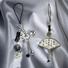 two necklaces with charms attached to them sitting on a satin surface in front of a silver sheet