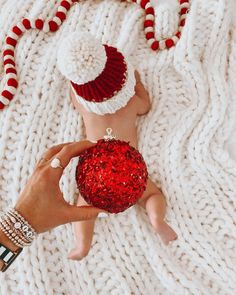 a person is holding a red ornament in their hand while laying on a white blanket