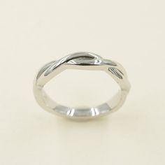 a white gold wedding ring with an intertwined design on the top, and a curved band