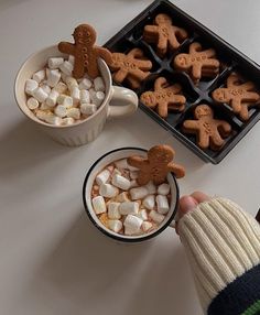 a person holding a cup filled with marshmallows and gingerbread cutouts