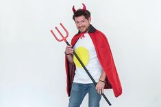 a man in devil costume holding a pitchfork and smiling at the camera while standing against a white background