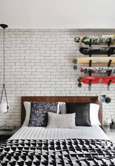 a bed with black and white bedspread in front of a brick wall that has skateboards on it