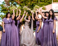 a group of women in purple dresses are holding flowers and posing for the camera with their hands up