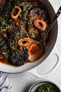 a white bowl filled with meat and carrots next to a spoon on top of a table