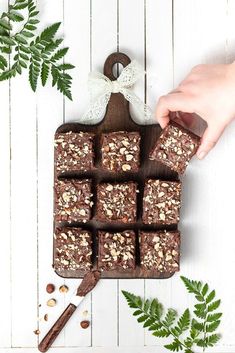 chocolate squares with nuts in the middle and green leaves around them on a white wooden background