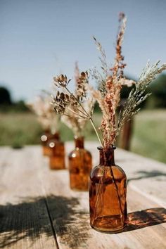 three vases with dried plants in them on a table outside, one is empty