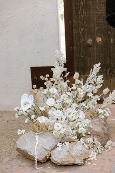 a bouquet of white flowers sitting on top of a rock next to a wooden door