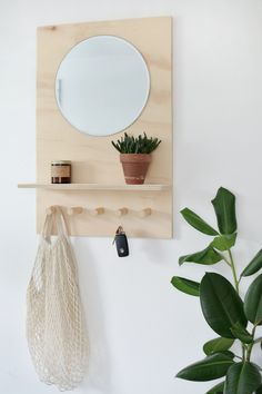 a wooden shelf with a mirror, potted plant and key holder on it next to a white wall